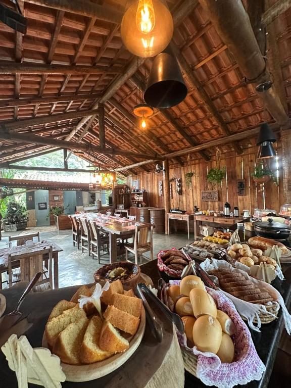 Salão do café da manhã com mesas de madeira, cestas de pães e bolo de fubá