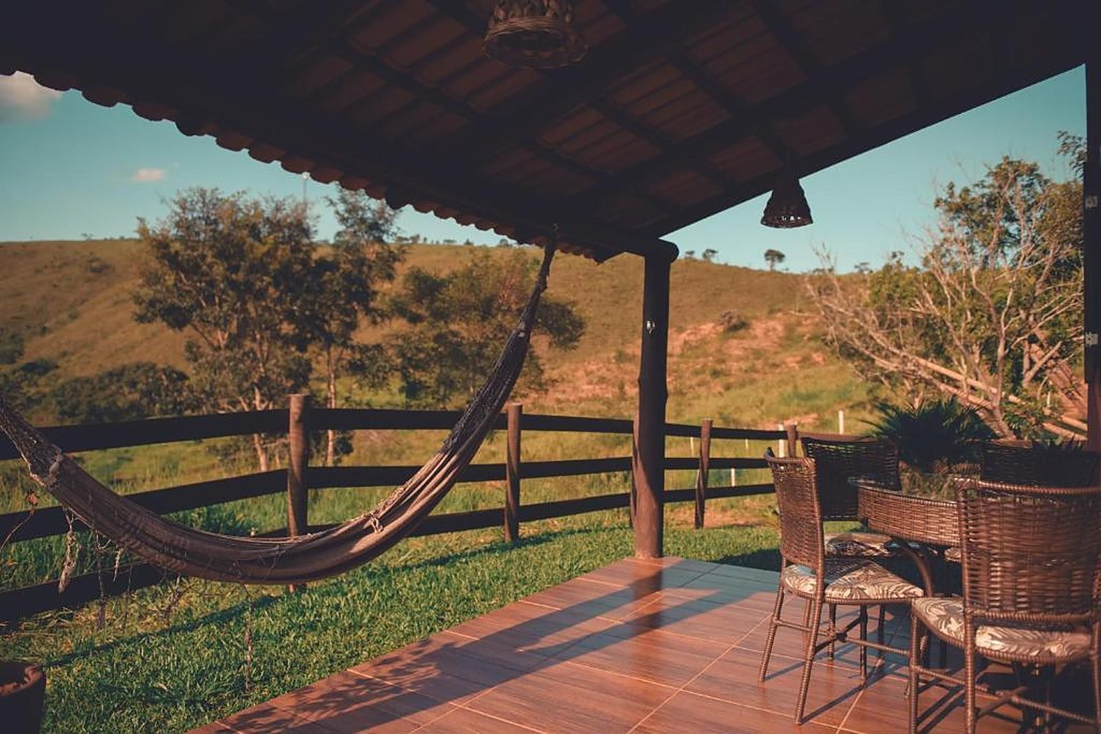 Varanda de chalé com rede, mesa e cadeiras, com vista para a serra